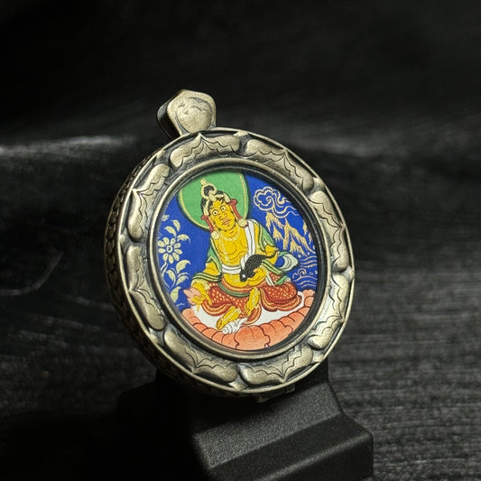 Angled view of the Yellow Jambhala mini thangka pendant showing detailed mineral pigment painting and the carved 925 silver protective case.