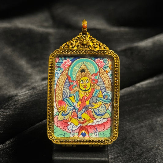 Front view of a Yellow Jambhala mini thangka pendant hand-painted with mineral pigments, depicting the Tibetan Buddhist wealth deity seated on a lotus throne, framed in an ornate gold-tone copper case with intricate Tibetan patterns.
