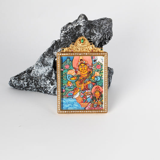 Front view of dual deity thangka pendant showing Yellow Jambhala with Vasudhara detail, crystal-style bezel border, and ornate top crown with green accent stone