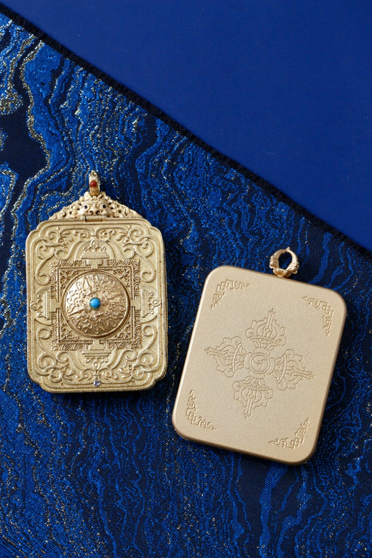 Back view of Zaki Lhamo mini thangka gawu pendant with embossed gold-tone copper case and turquoise-style center detail on blue brocade background.