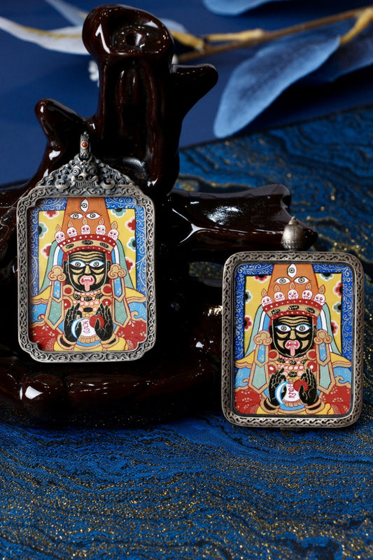 Two Zaki Lhamo hand-painted mini thangka pendants in different 925 silver cases, staged on a dark sculpture with blue textile backdrop