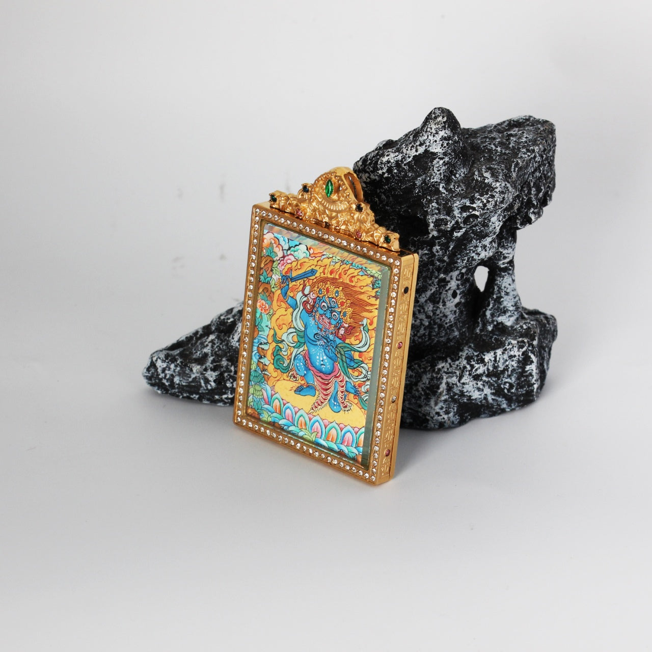 Angled view of Acalanatha (Fudo Myo-o) mini thangka pendant showing the thickness and structure of the double-sided titanium steel case, ornate top crest with green stone detail, and vivid hand-painted artwork