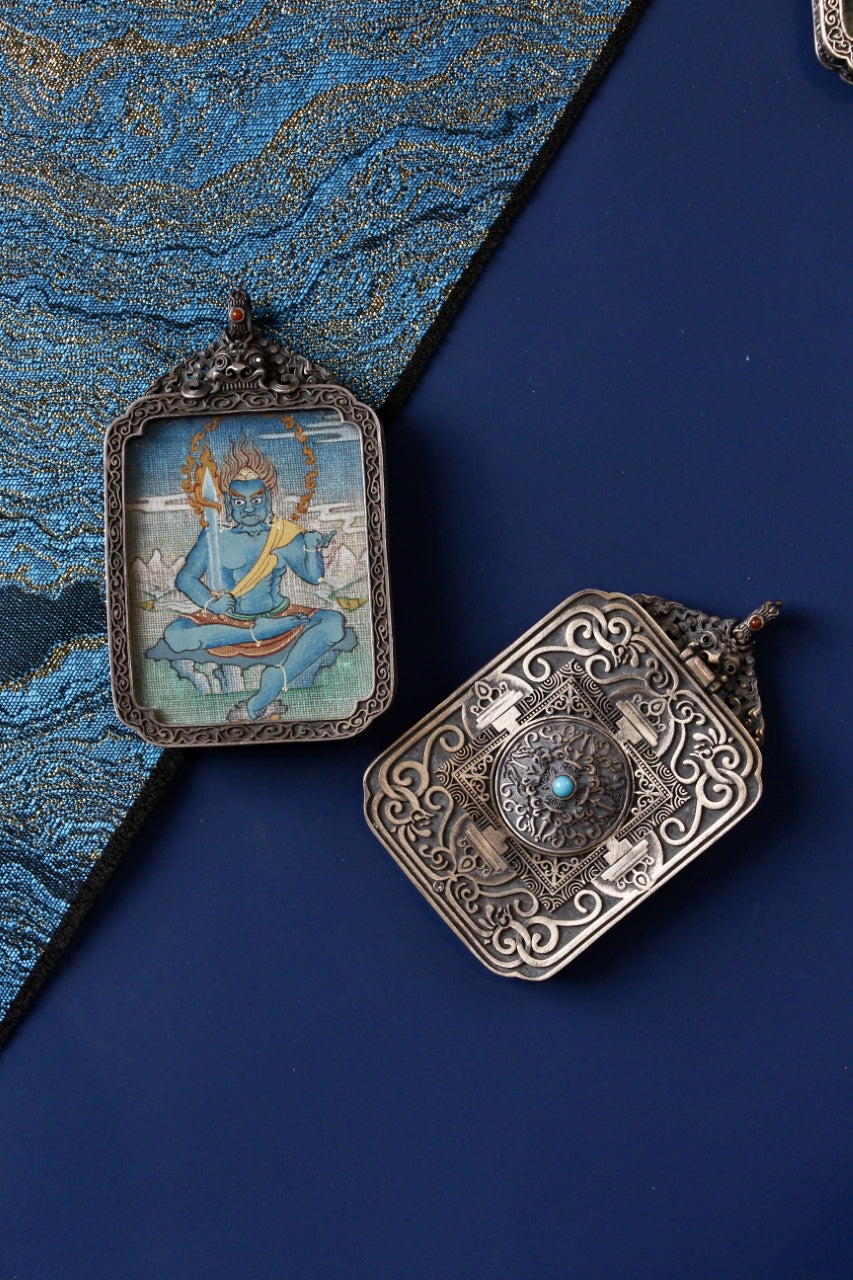Front-and-back view of an Acalanatha (Fudo Myo-o) mini thangka pendant, fully hand-painted with mineral pigments, set in a vintage silver gawu box on a blue textile background.