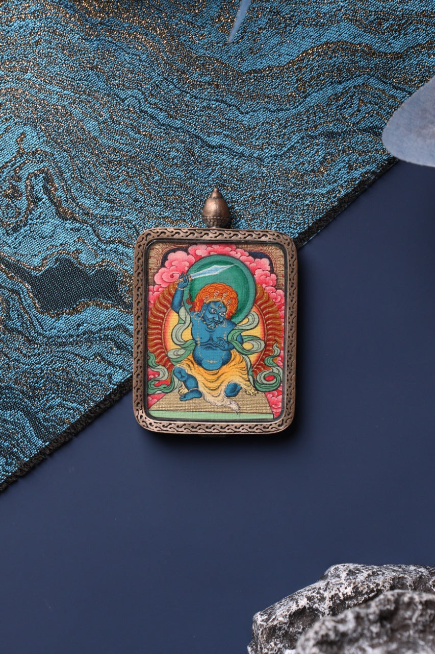 Close-up view of the hand-painted Acalanatha mini thangka pendant, showing detailed mineral pigment colors and traditional Tibetan iconography