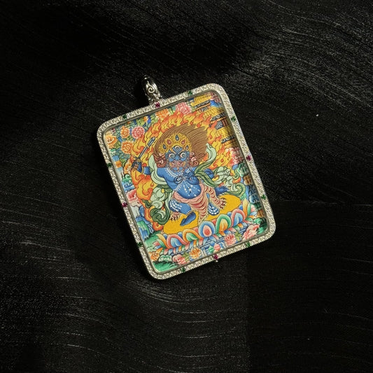 Close-up view of the Acalanatha mini thangka pendant featuring the fierce blue Acalanatha deity holding a sword, surrounded by flames and floral motifs, hand-painted with mineral pigments inside a square silver pendant frame.