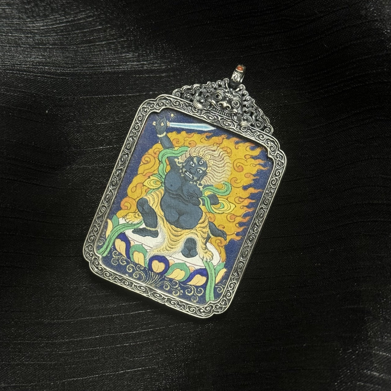 Detailed view of the vintage silver case and frame edges of the Acalanatha thangka pendant, highlighting traditional metalwork and protective structure.