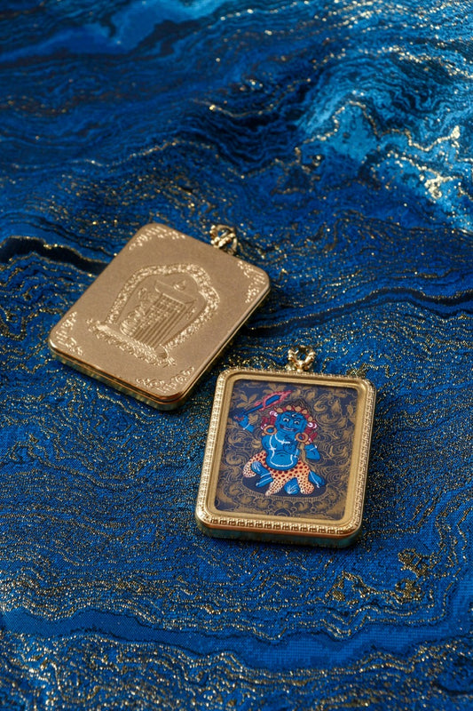 Acalanatha (Fudo Myo-o) mini thangka pendant showing the front black-gold painting and the engraved metal back case on blue brocade fabric