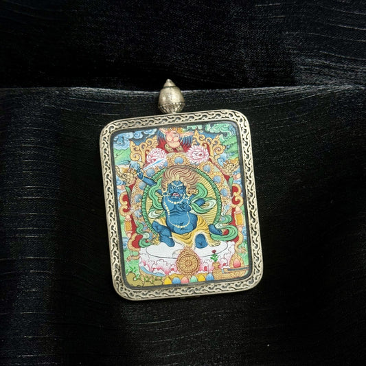 Angled close-up of Acalanatha miniature thangka pendant highlighting raised sword, dynamic posture, blue wrathful expression, layered mineral pigments, and carved silver gawu frame.