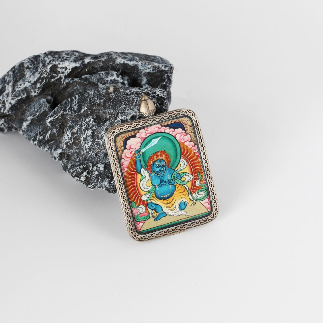 Angled view of Acalanatha mini Thangka pendant showing the hand-painted wrathful deity details, layered mineral pigment colors, and the ornate engraved silver border around the rectangular pendant.