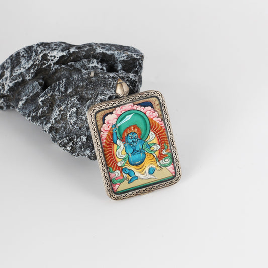 Angled view of Acalanatha mini Thangka pendant showing the hand-painted wrathful deity details, layered mineral pigment colors, and the ornate engraved silver border around the rectangular pendant.