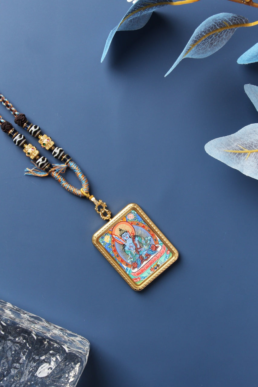 Akasagarbha Bodhisattva mini thangka pendant shown at an angle, featuring the hand-painted deity image with mineral pigment colors, rectangular metal case with textured raised border, and top clasp-to-bail hardware connection.