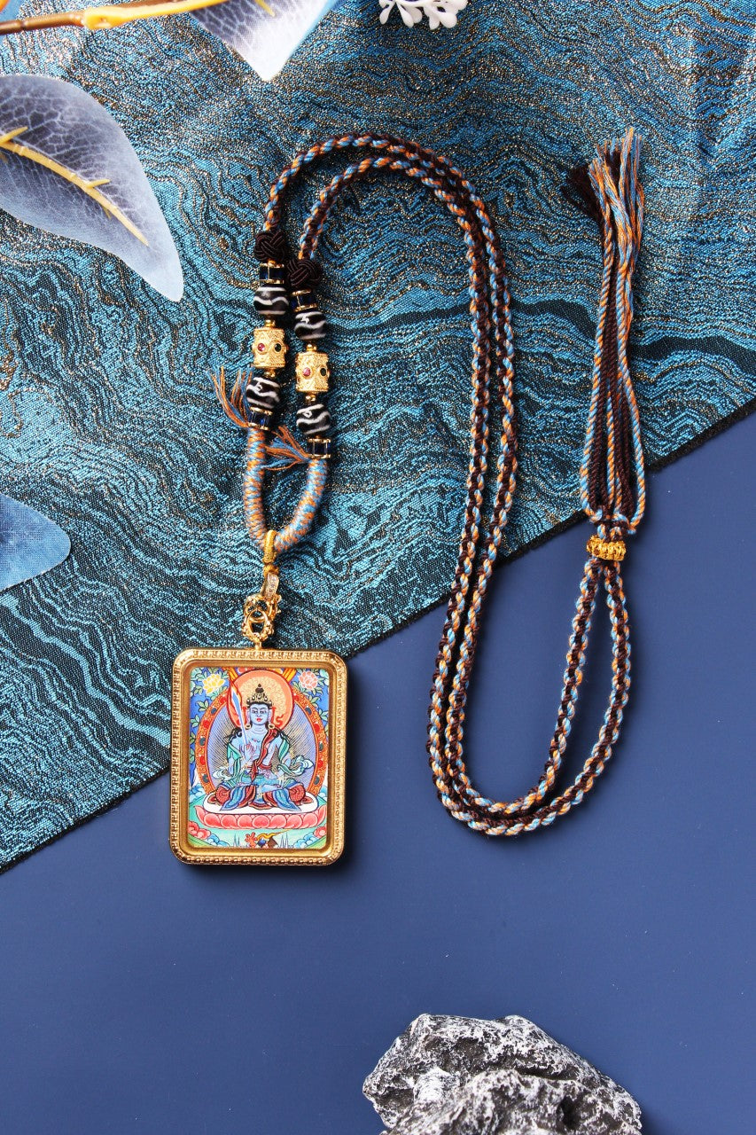 Full view of the Akasagarbha Bodhisattva mini thangka pendant showing the front painting, rectangular metal case, braided cord, bead section with patterned round beads, gold-tone spacer details, and the adjustable cord ends.