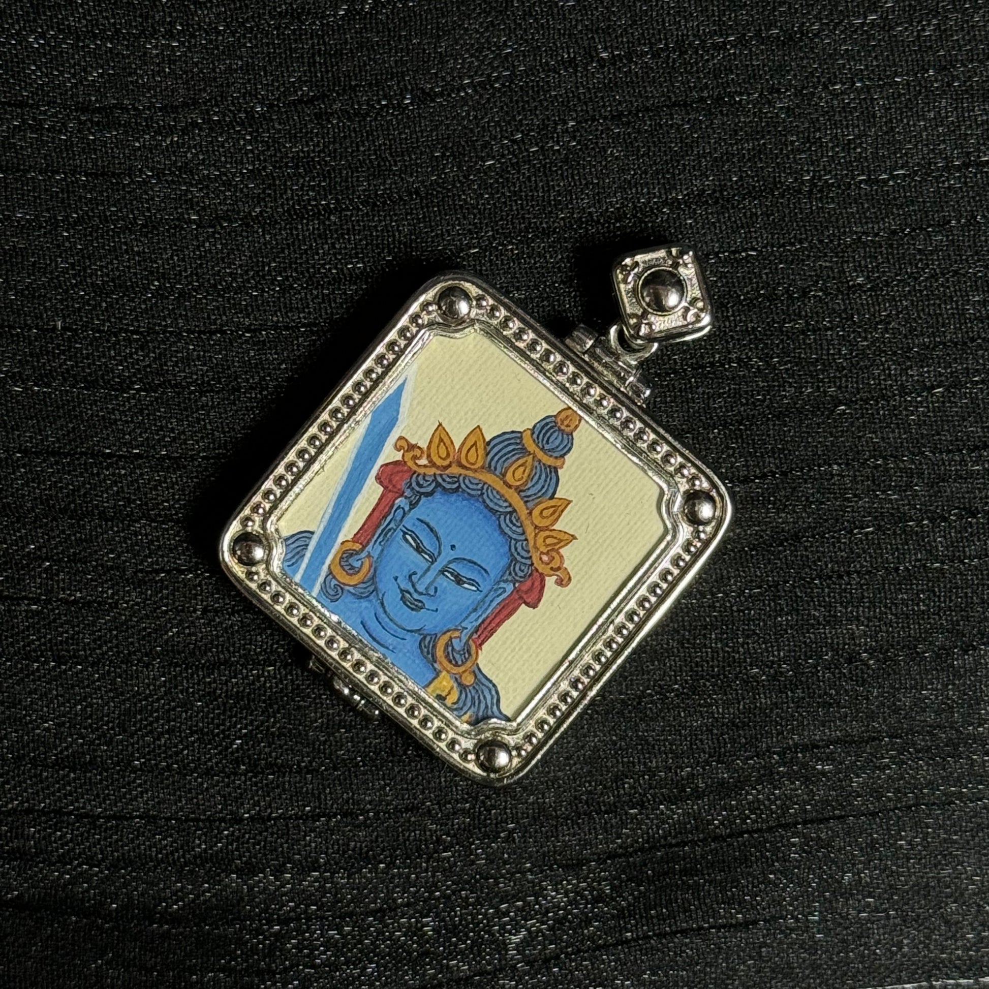 Close-up detail of the Akashagarbha Bodhisattva portrait in a miniature thangka pendant, showing mineral pigment painting and silver framed setting.