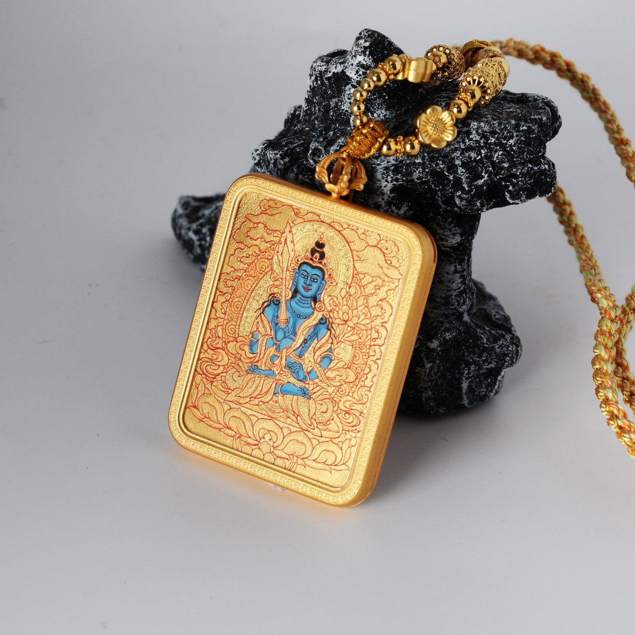 Close-up of an Akashagarbha Bodhisattva mini thangka pendant showing braided cord, decorative metal beads, and the handcrafted hanging structure with the gold-ground painting panel.