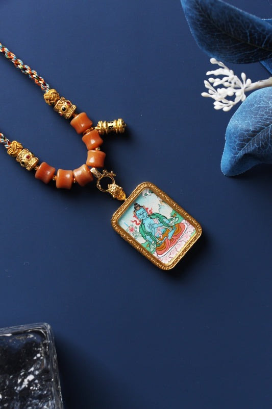Angled close-up of Akashagarbha Bodhisattva mini thangka pendant showing mineral pigment hand-painting, rectangular textured metal bezel, and bead-and-braided cord necklace details