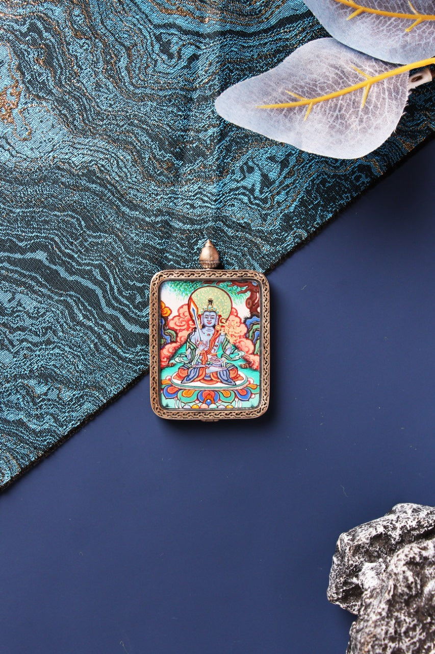 Front view of Akashagarbha Bodhisattva mini thangka pendant, fully hand-painted with mineral pigments, set in a dark-toned sterling silver case with Dunhuang Nine-Color Deer-inspired edging and a domed top, photographed on a navy surface with blue brocade fabric, translucent leaf decor, and a stone prop.