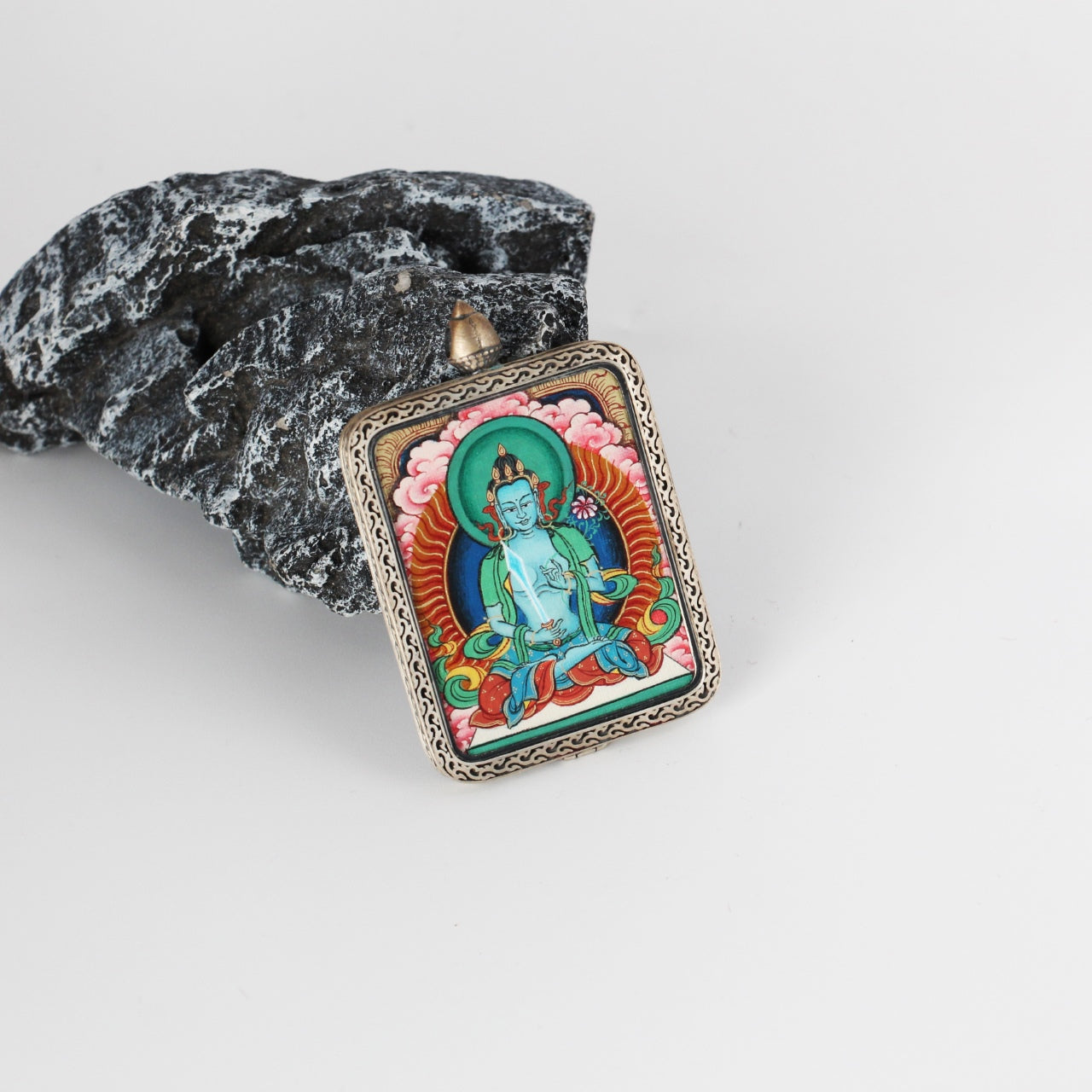 Tilted view of an Akashagarbha Bodhisattva mini Thangka pendant, highlighting the layered mineral pigment colors, refined line work, and engraved silver gawu-style frame.