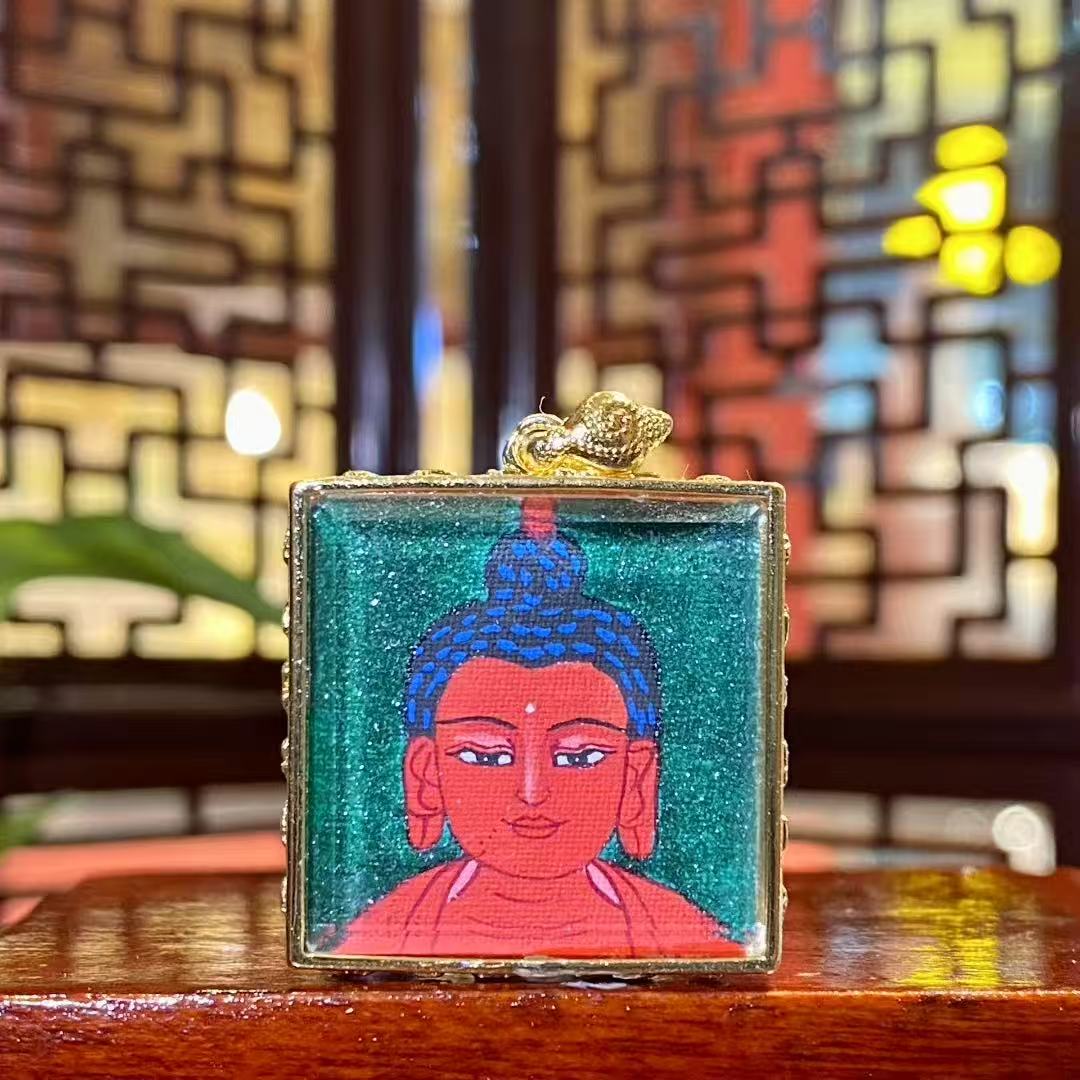 Front view of hand-painted Amitabha Buddha mini thangka in a gold-plated copper Gau pendant, featuring a serene Buddha portrait on a green background