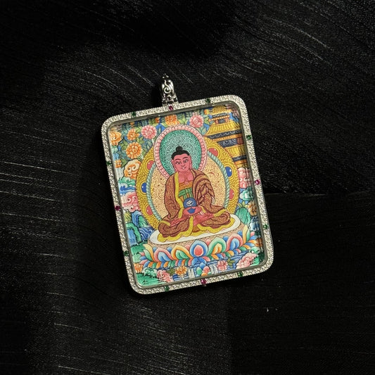 Close view of a hand-painted Amitabha Buddha miniature thangka pendant, showing the Buddha seated on a lotus base with traditional Tibetan floral background and intricate mineral pigment colors inside a square pendant frame.