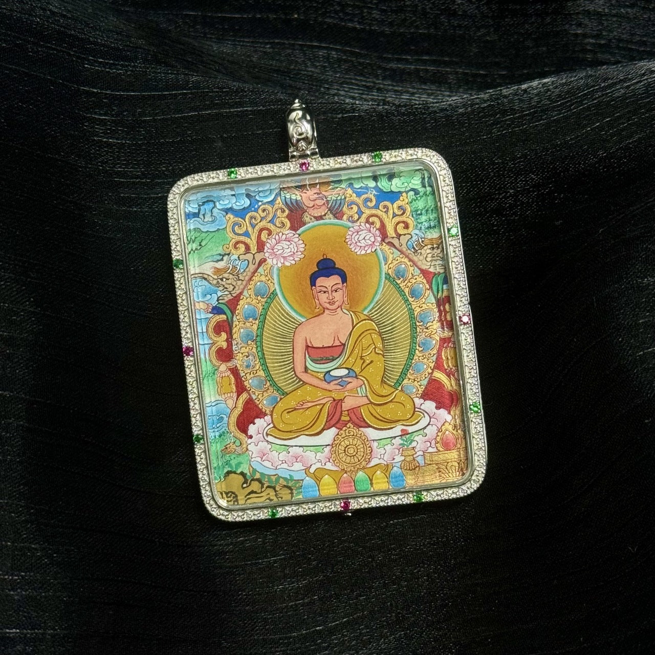 Angled close-up of Amitabha Buddha miniature thangka pendant highlighting calm facial expression, golden halo, lotus base, layered mineral pigments, and jeweled silver gawu casing.