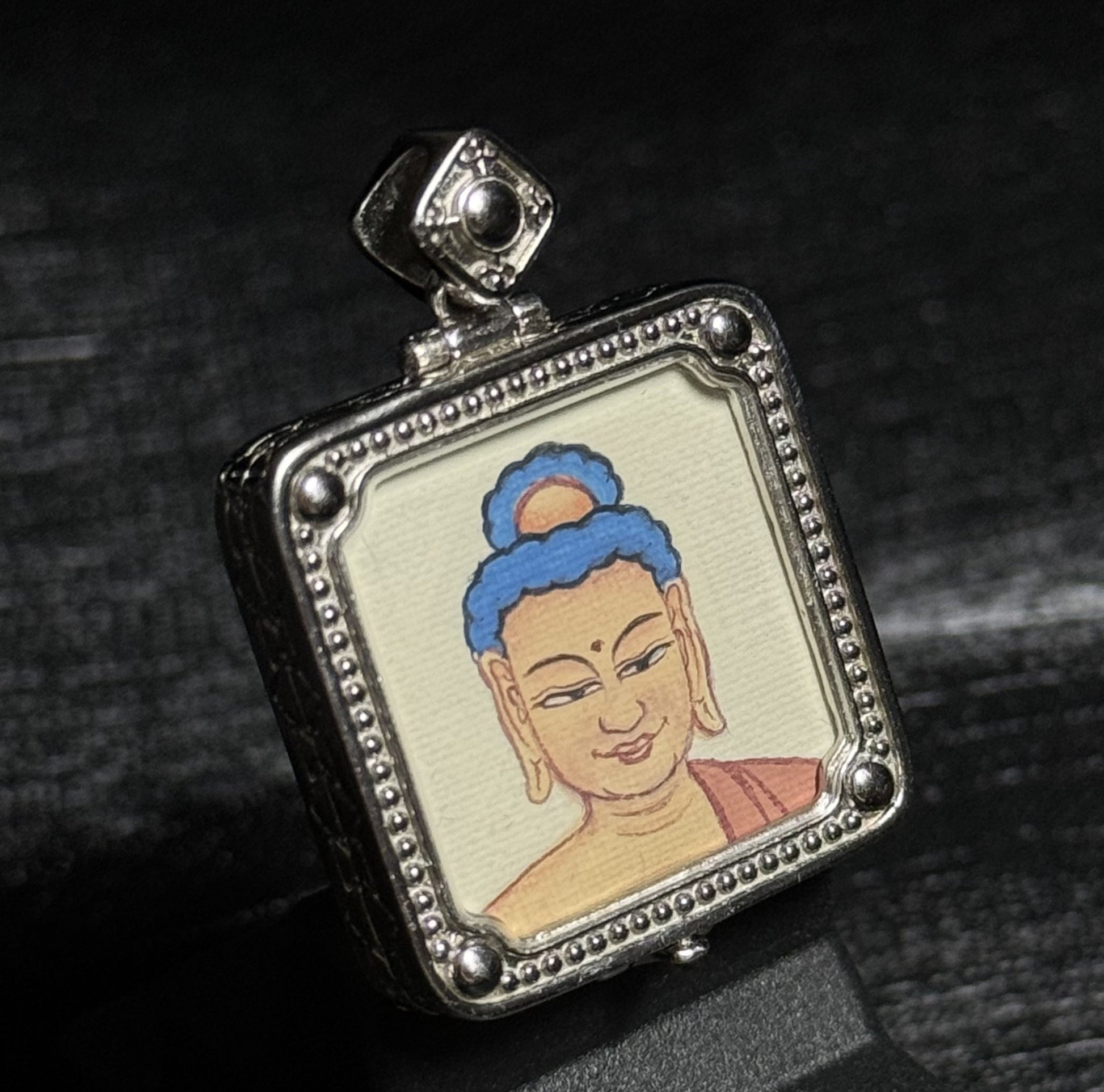 Detailed view of the Amitabha Buddha portrait in a miniature thangka pendant, showing mineral pigment painting and silver framed setting.