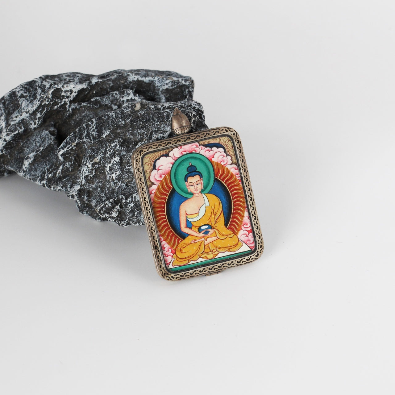Amitabha Buddha mini Thangka pendant displayed on a stone prop, highlighting the hand-painted artwork, bright pink cloud background, and the detailed engraved pure silver frame.