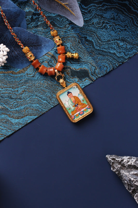 Rectangular Amitabha Buddha mini thangka pendant on a braided cord necklace, showing hand-painted deity artwork in a gold-toned frame with bead accents