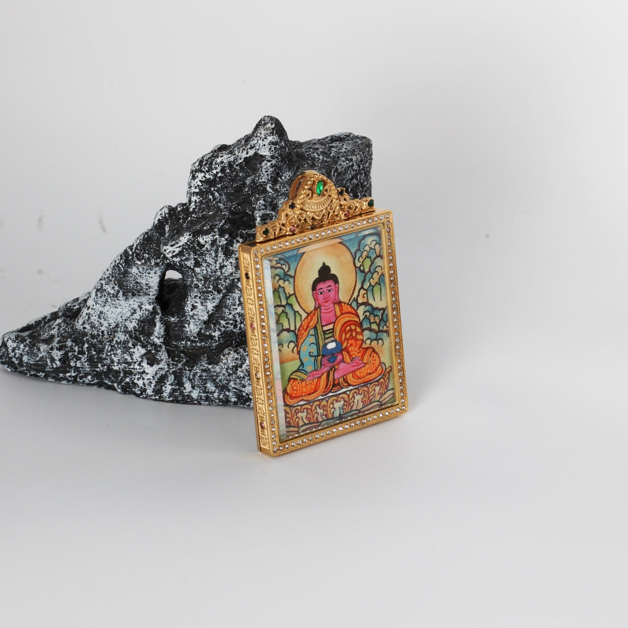 Side-angled photo of Amitabha Buddha mini thangka pendant showing the gold-tone titanium steel case profile, crystal border around the front window, and the hand-painted Amitabha Buddha image inside.
