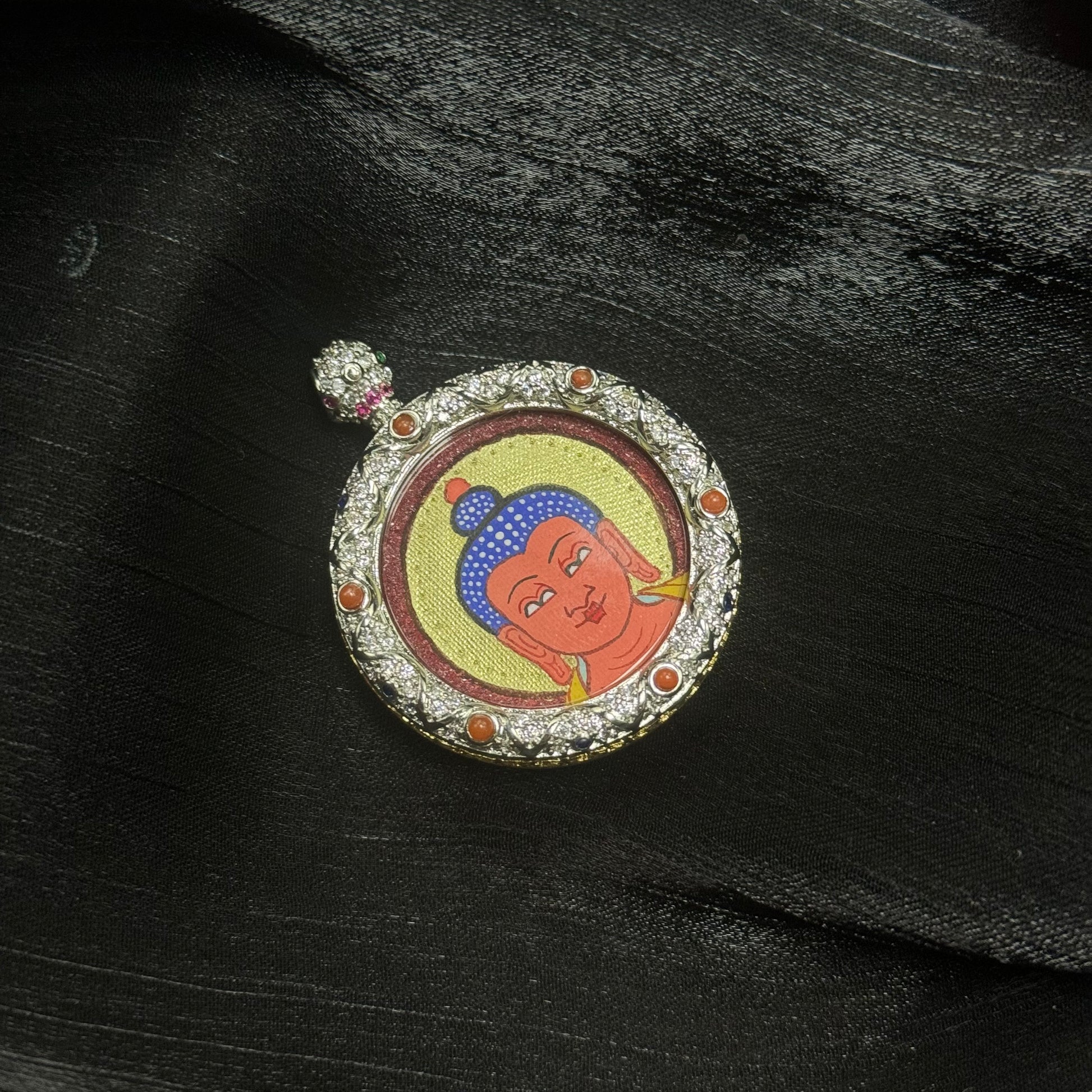 Angled view of Amitabha Buddha miniature thangka pendant highlighting cinnabar red background texture, layered gold halo painting, and decorative gemstone copper frame
