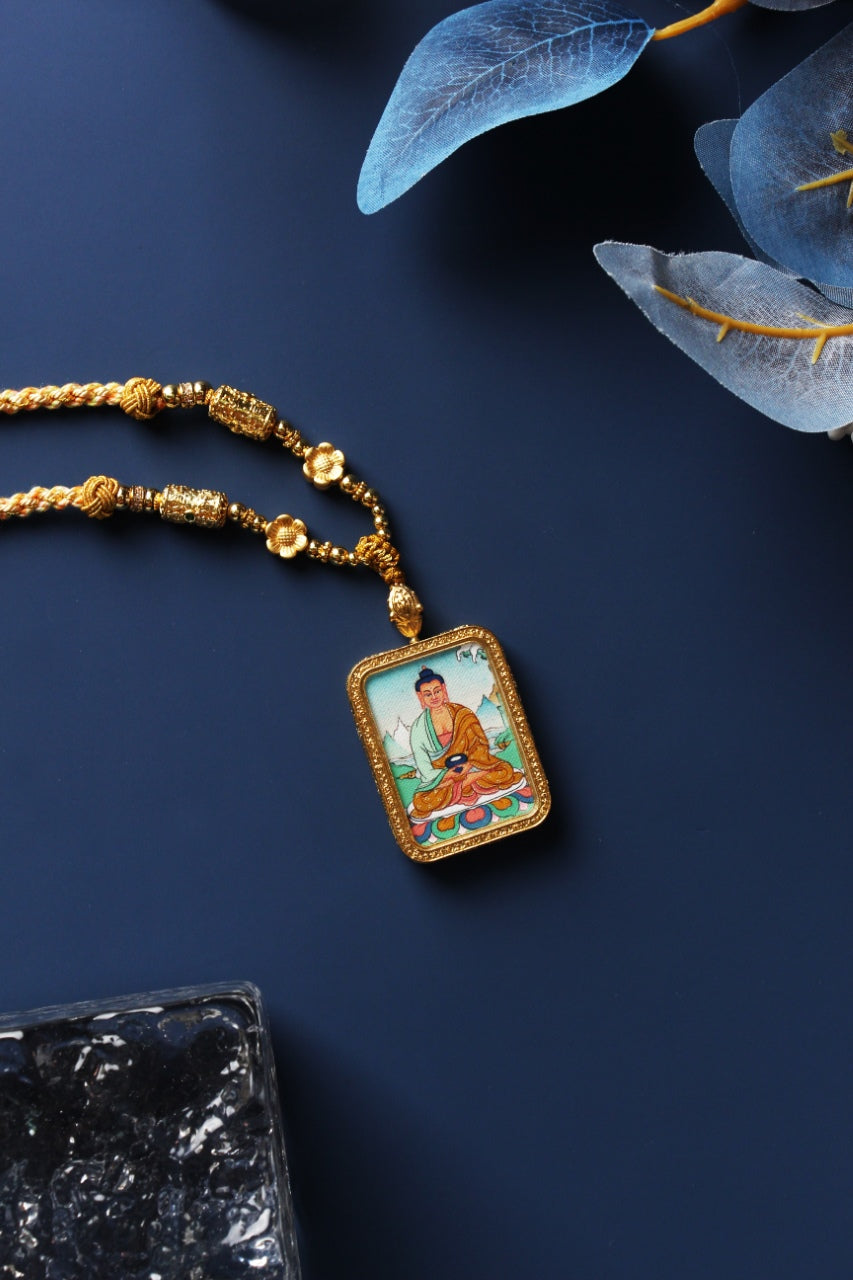 Amitabha Buddha thangka pendant necklace laid flat, featuring braided cord, gold-tone metal beadwork, and a rectangular framed pendant