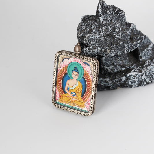 Angled view of Amitabha Buddha mini Thangka pendant showing the layered mineral pigment colors, fine facial detailing, and the ornate engraved silver border around the rectangular pendant.