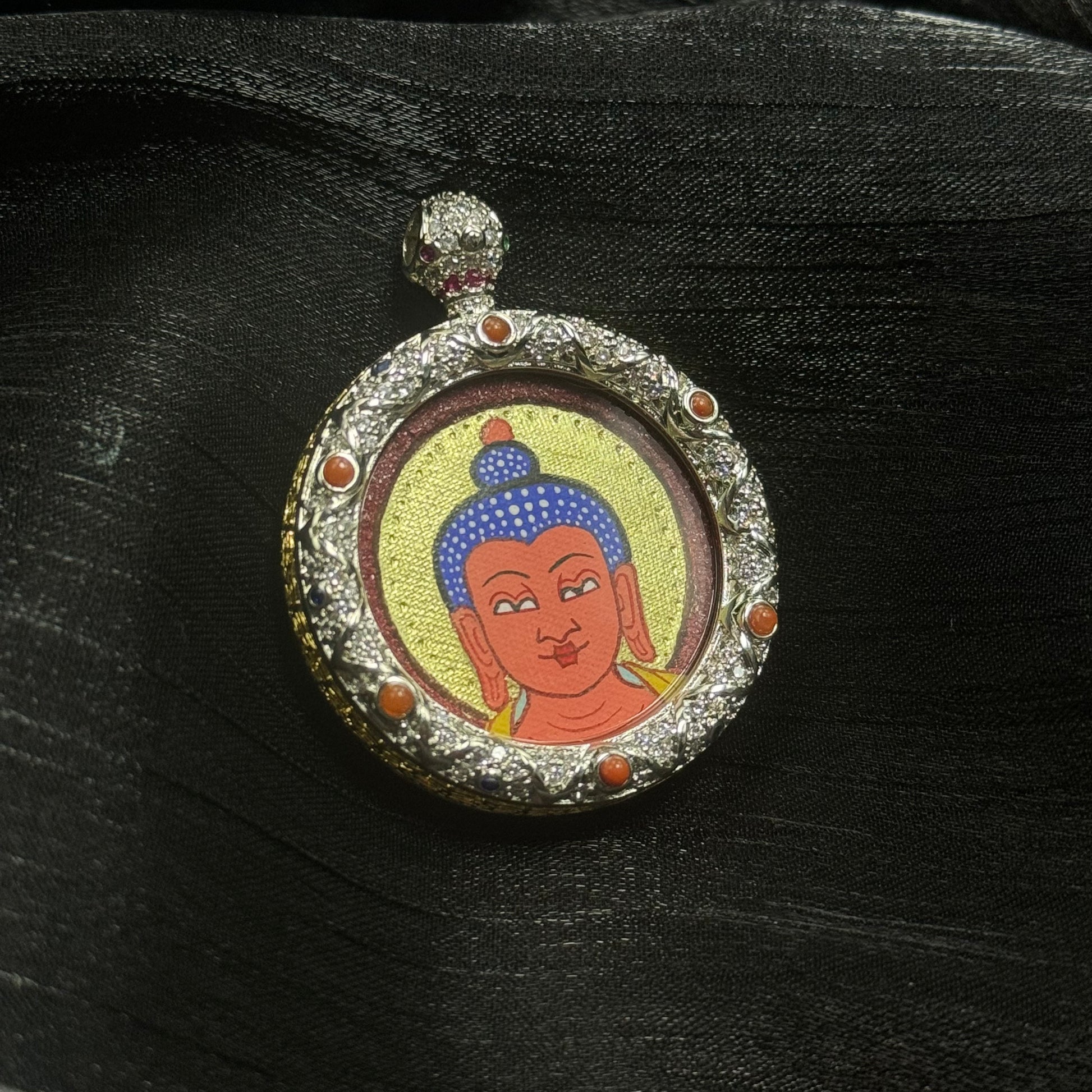 Amitabha Buddha miniature thangka pendant showing hand-painted Buddha head with gold halo and cinnabar background framed in decorative gemstone copper pendant setting