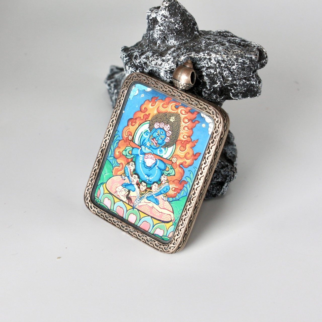 Angled view showing depth and layered mineral pigments of Bernagchen Black Cloaked Mahakala mini thangka pendant, hand-painted Rebgong thangka set in silver gawu-style case