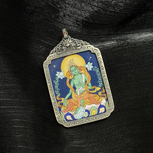 Angled view of a Green Tara mini thangka pendant showing layered mineral pigment texture, detailed lotus seat, and engraved silver frame.