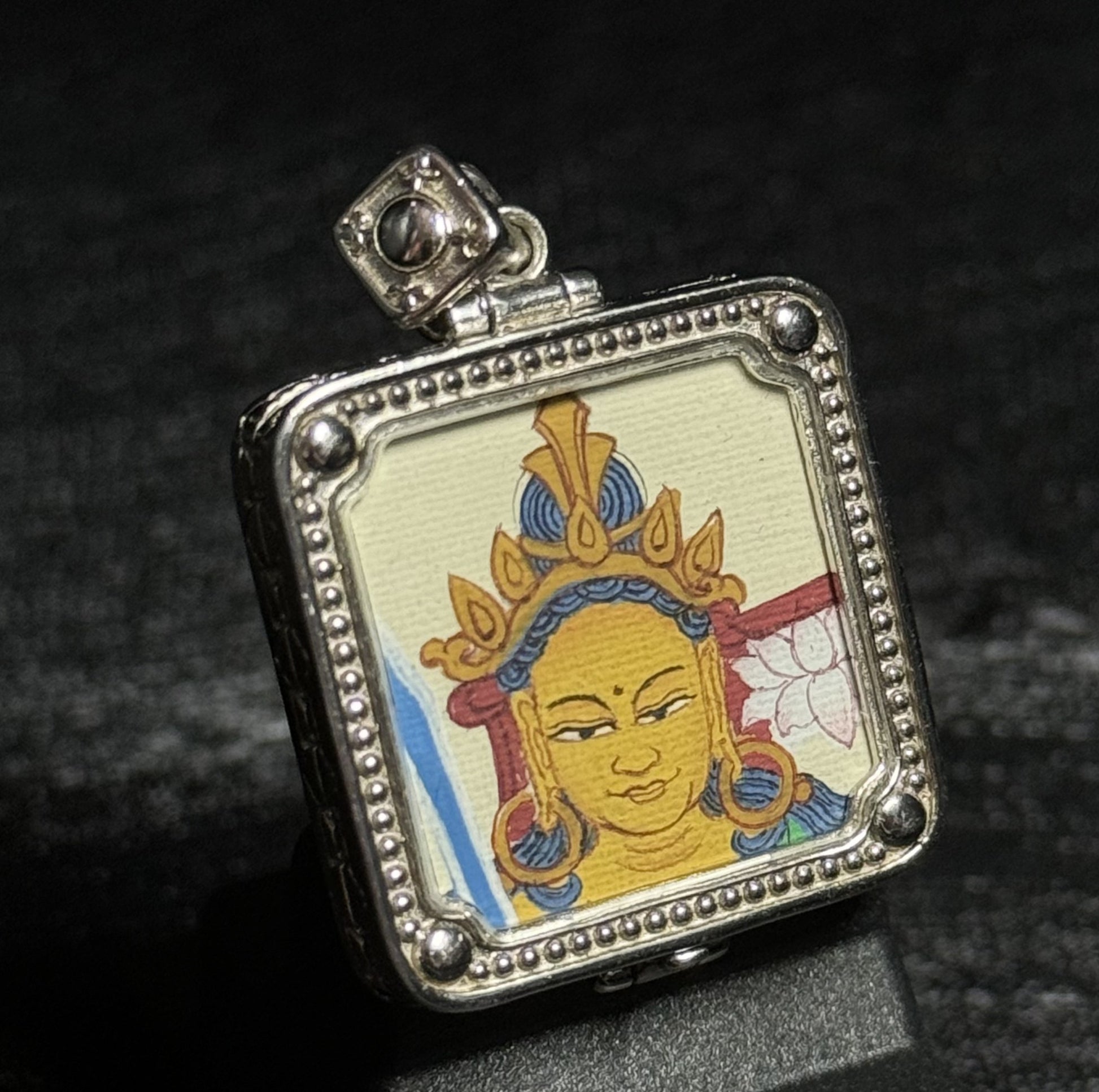 Angled view of a miniature Manjushri Bodhisattva thangka pendant highlighting the hand-painted deity portrait and textured silver pendant frame.