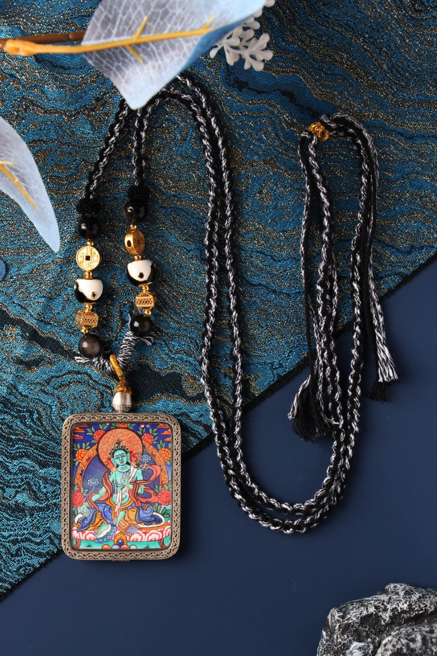 Full display of Green Tara mini thangka pendant necklace with braided cord and beads, silver-plated case, and front painting on a blue background