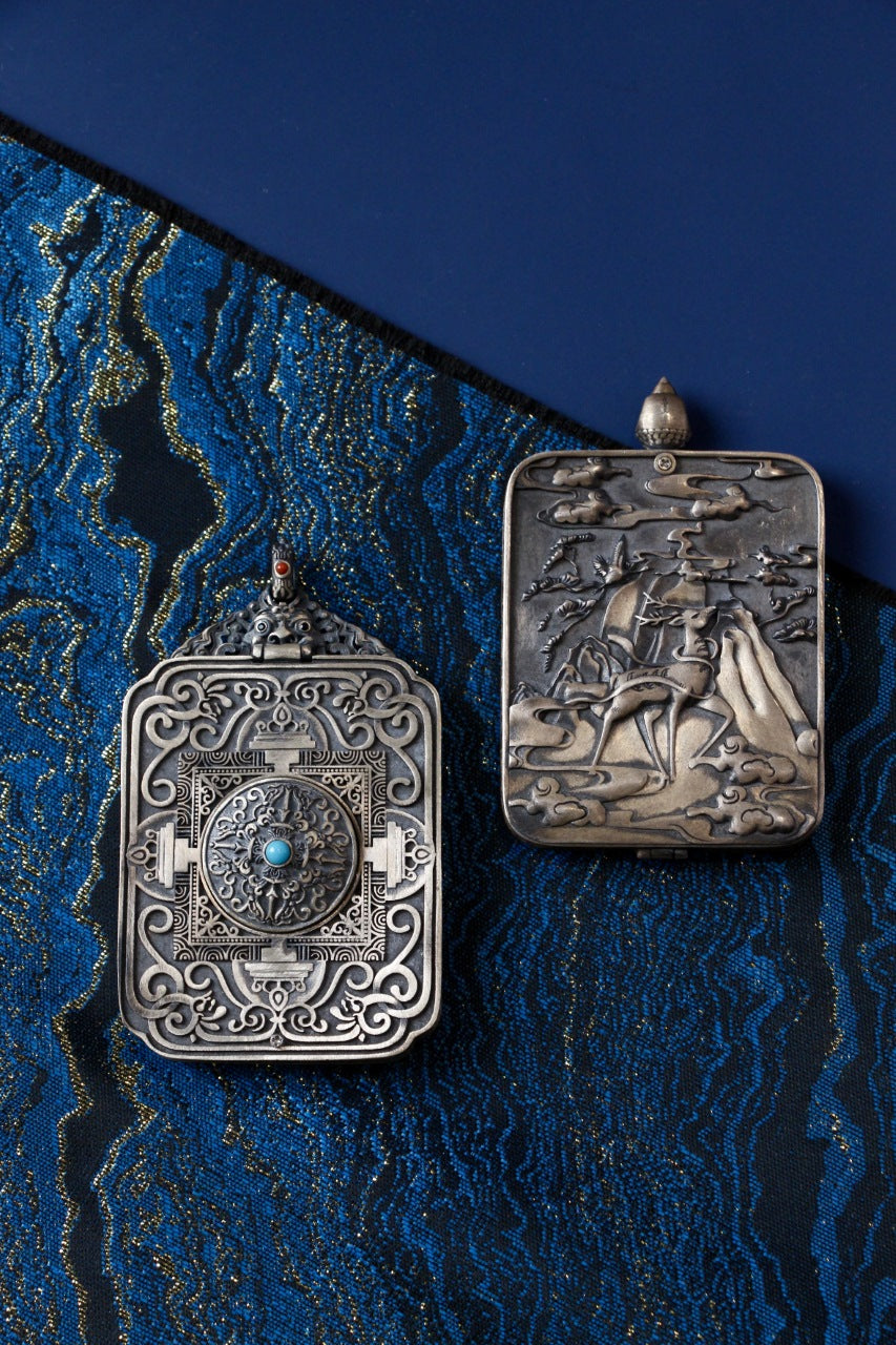 Back view of two 925 silver mini thangka pendant cases showing engraved metalwork designs and inlay details on blue brocade background
