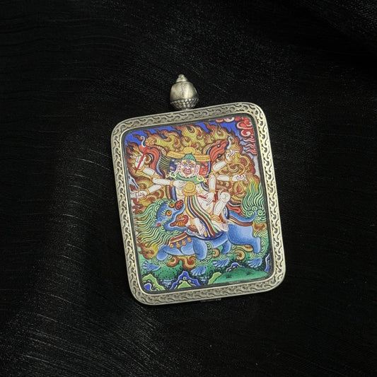 Angled view of Baihar protector deity thangka pendant showing layered mineral pigment textures and traditional silver frame craftsmanship