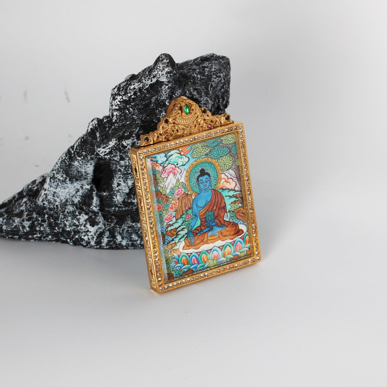 Angled view of Bhaisajyaguru Buddha mini thangka pendant showing the thickness and structure of the titanium steel case, with detailed hand-painted Nepalese thangka artwork visible inside