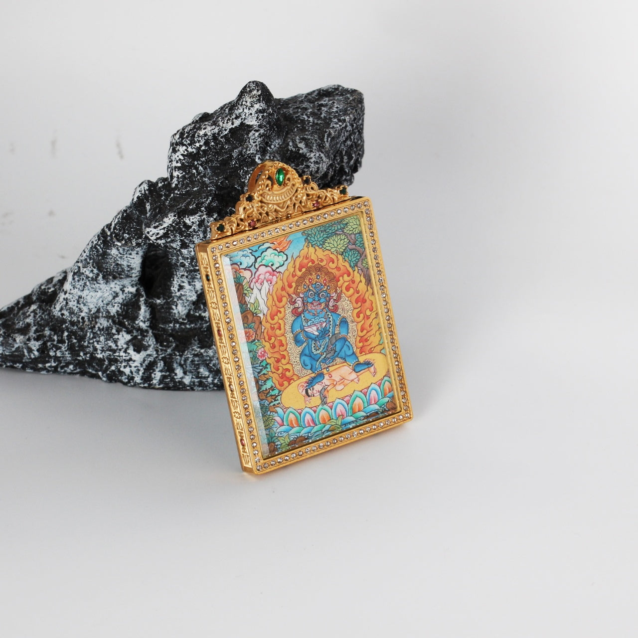 Angled view of Black Jambhala mini thangka pendant showing the thickness and structure of the titanium steel case, with ornate top crest and detailed hand-painted thangka artwork visible inside
