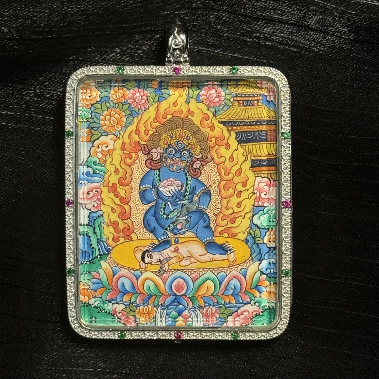 Detailed close-up of a Black Jambhala mini thangka pendant highlighting the fierce expression of the deity, intricate lotus pedestal, and richly colored mineral pigment painting.
