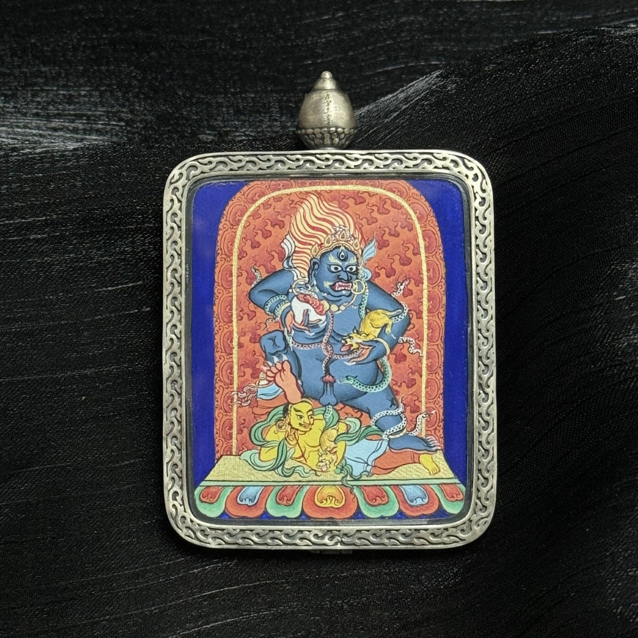 Close-up detail of Black Jambhala wealth deity miniature thangka, hand-painted Tibetan artwork with vivid mineral pigments in silver frame.