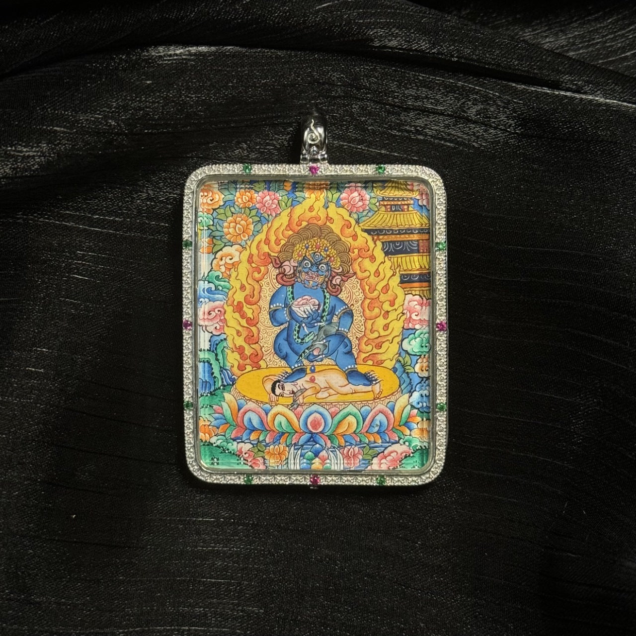 Hand-painted Tibetan Black Jambhala miniature thangka pendant depicting the wealth deity with flaming halo, lotus throne, and vibrant mineral pigment colors.