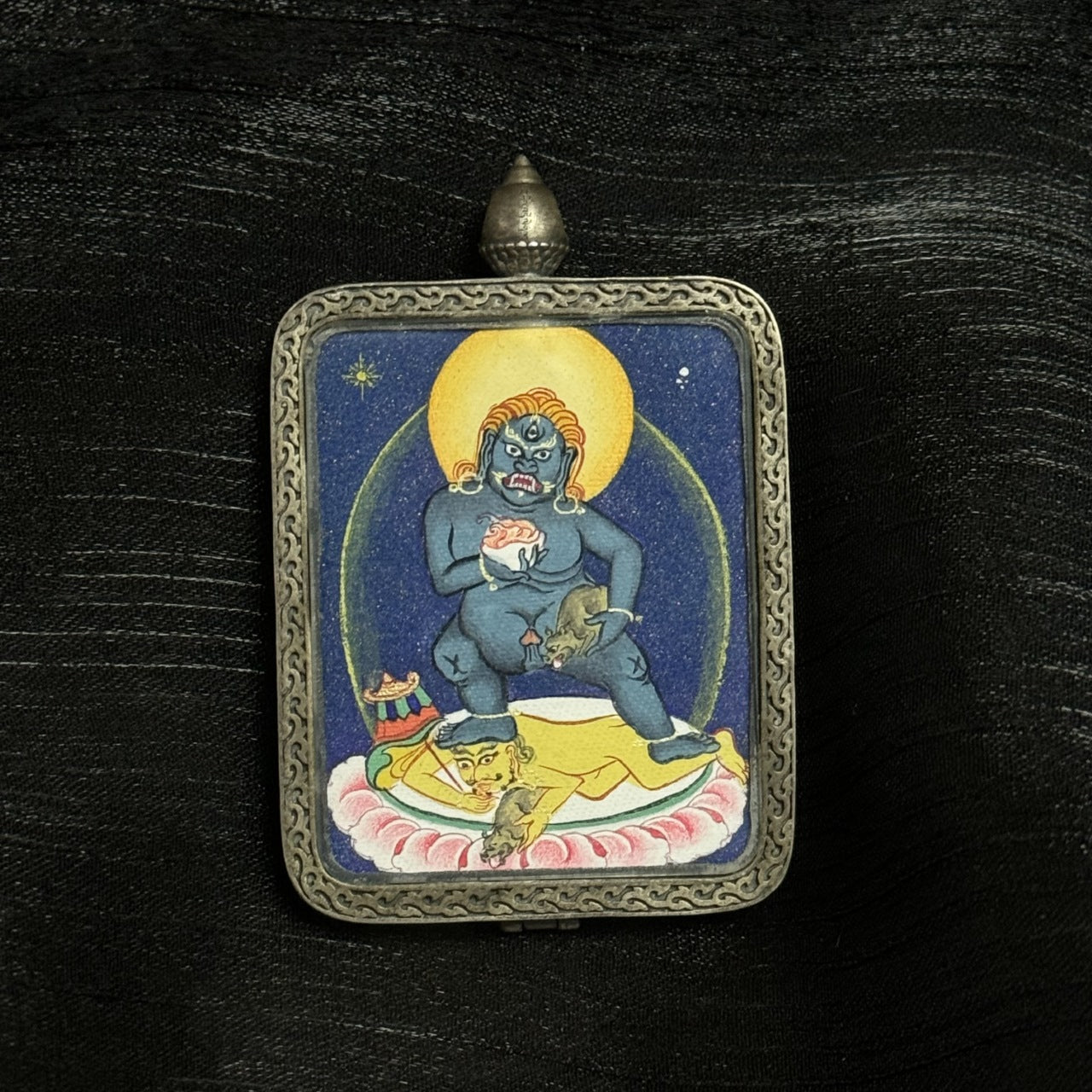 Detailed front view of Black Jambhala Tibetan thangka pendant featuring authoritative deity iconography, coarse mineral pigment application, and silver frame craftsmanship