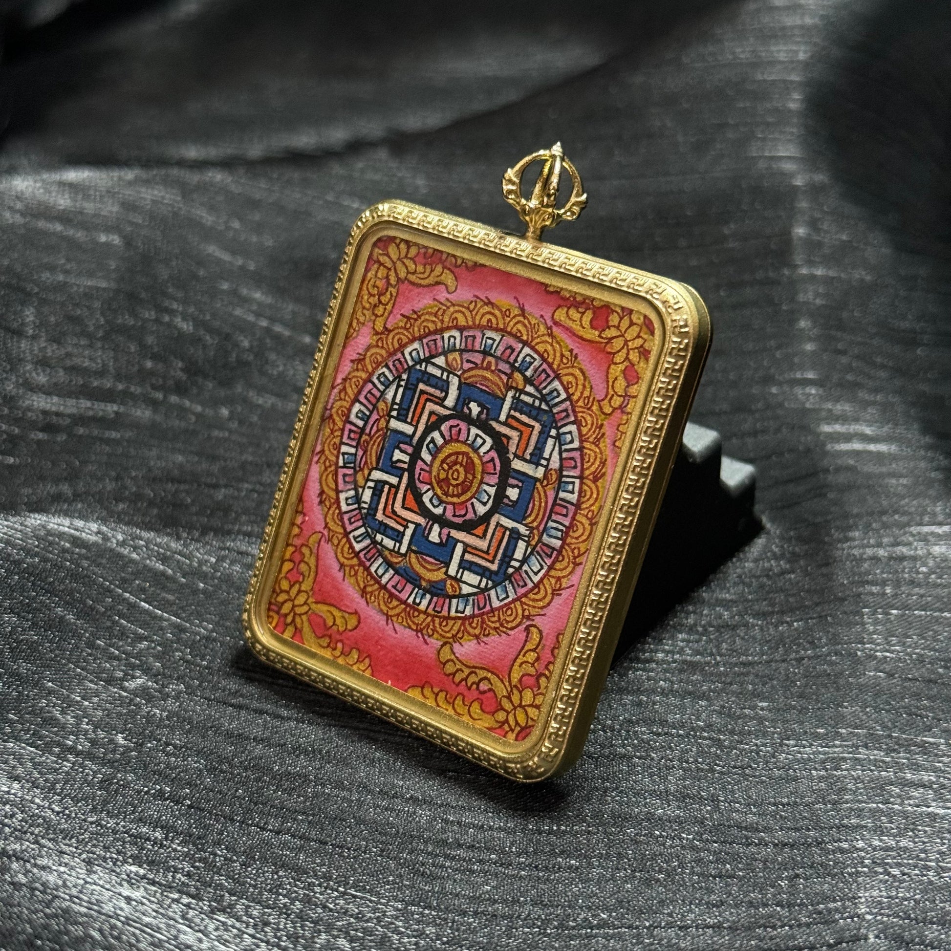 Front view of a Buddhist mandala miniature thangka pendant featuring symmetrical sacred geometry surrounded by traditional decorative motifs.