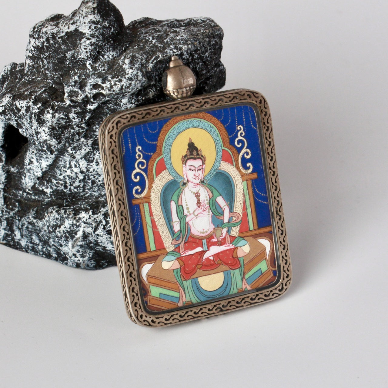 Angled view of the Vajrasattva mini thangka pendant highlighting the thickness of the sterling silver case, patterned edgework, and vivid mineral pigment colors.