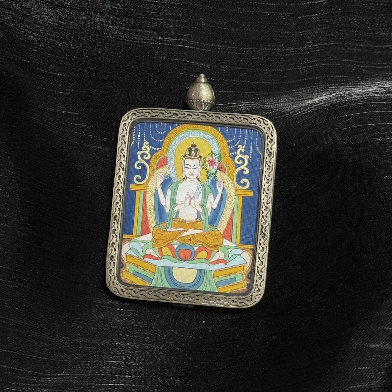 Close-up of Four-Armed Avalokiteshvara thangka artwork featuring detailed mineral pigment painting and ornate silver gawu pendant inspired by Dunhuang Nine-Color Deer motifs