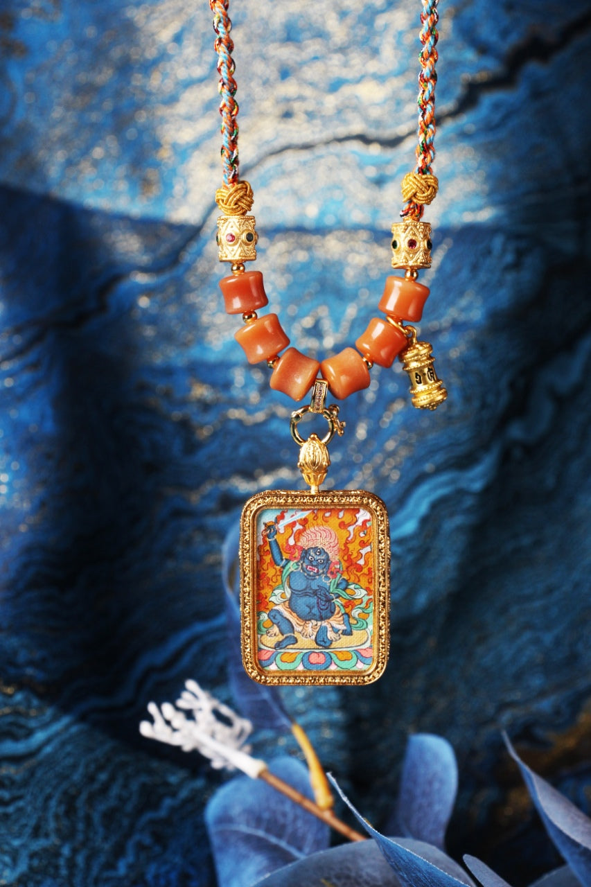 Close-up of Acalanatha mini thangka pendant necklace focusing on the multicolor braided cord, metal beadwork, orange beads, pendant connector, and rectangular framed painting