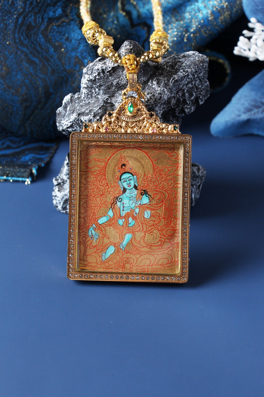 Close-up of Green Tara mini thangka pendant showing gold-ground line patterns, turquoise-blue deity figure, crystal-bordered square frame, and ornate top crown setting