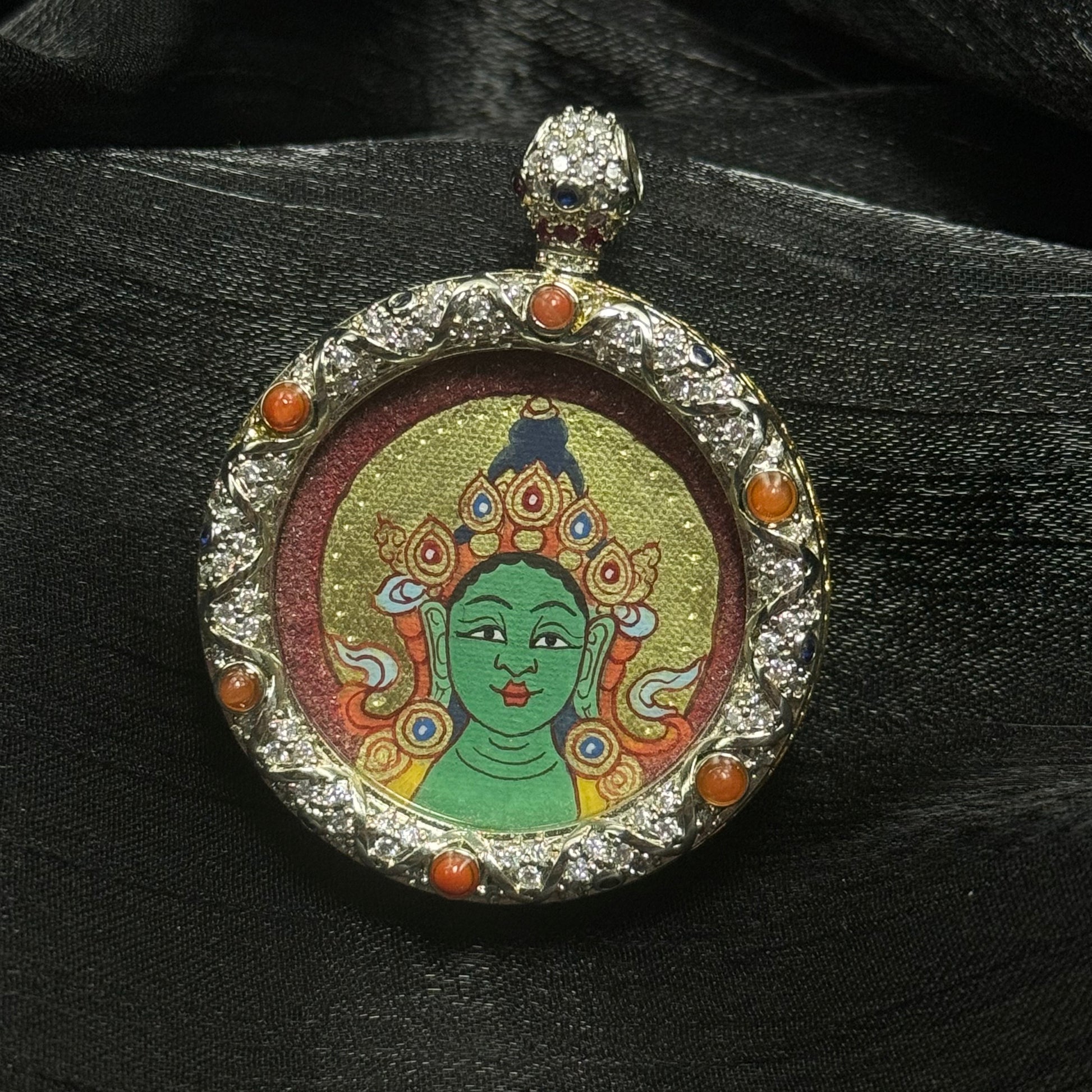 Close-up view of a hand-painted Green Tara miniature thangka portrait with green complexion, elaborate crown and gold background, mounted inside a decorative jeweled copper pendant frame with gemstone accents.